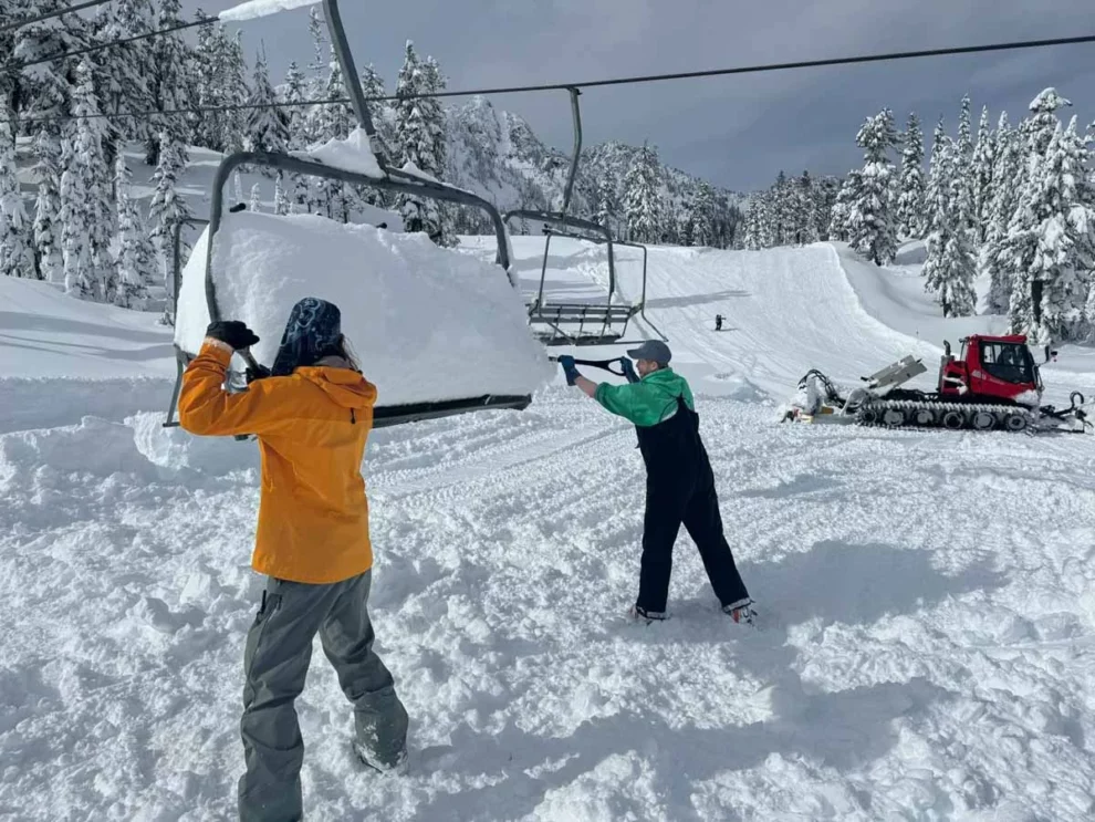 two shovel deep snow from a chairlift chair
