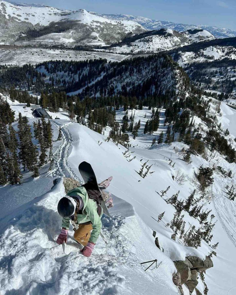 snowboarder climbs along steep ridgeline, board on back