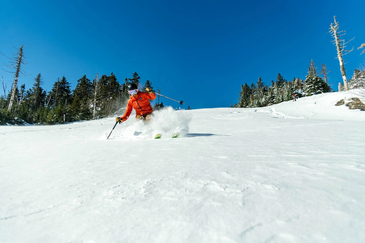 skier in red skips down fresh snowy slope, under a blue sky