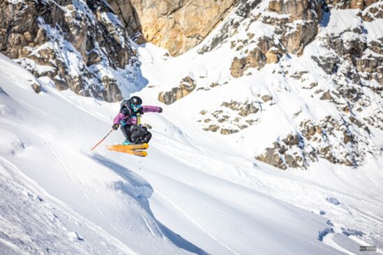 Skier performing a jump on snowy terrain with rocky peaks in Val d'Isère.