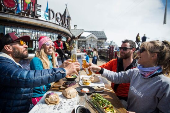 Group of friends enjoying après ski drinks at a lively outdoor bar in Val d'Isère