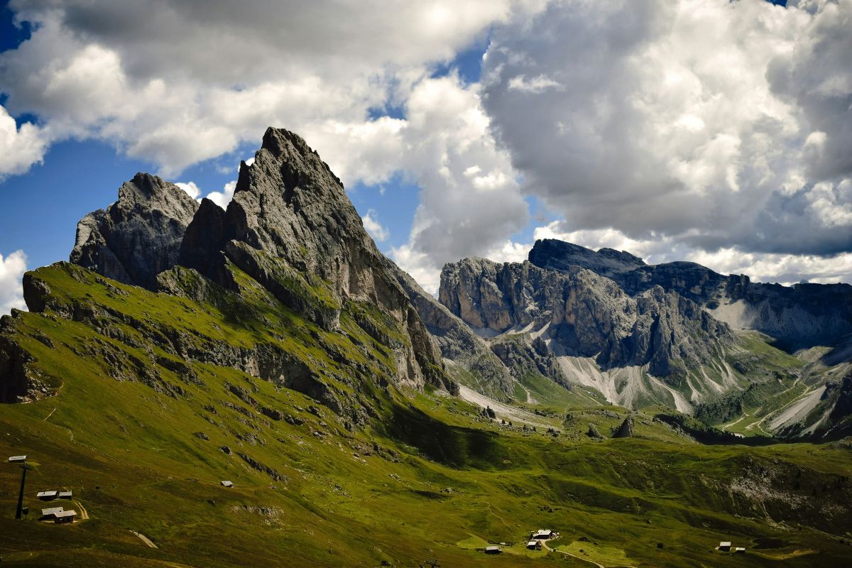 Dramatic mountain peaks and lush green meadows in Val Gardena, South Tyrol, under a partly cloudy sky.