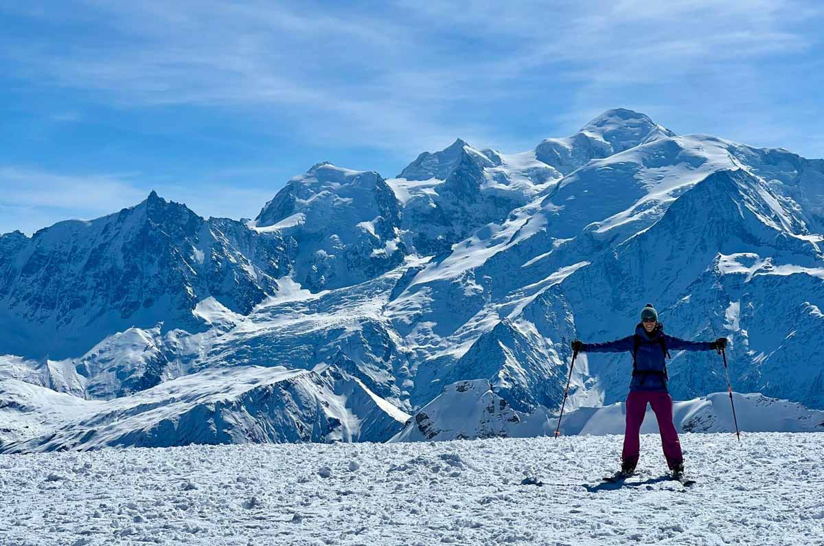 skier stands on plateau - a huge mountain backdrop behind - with arms spread