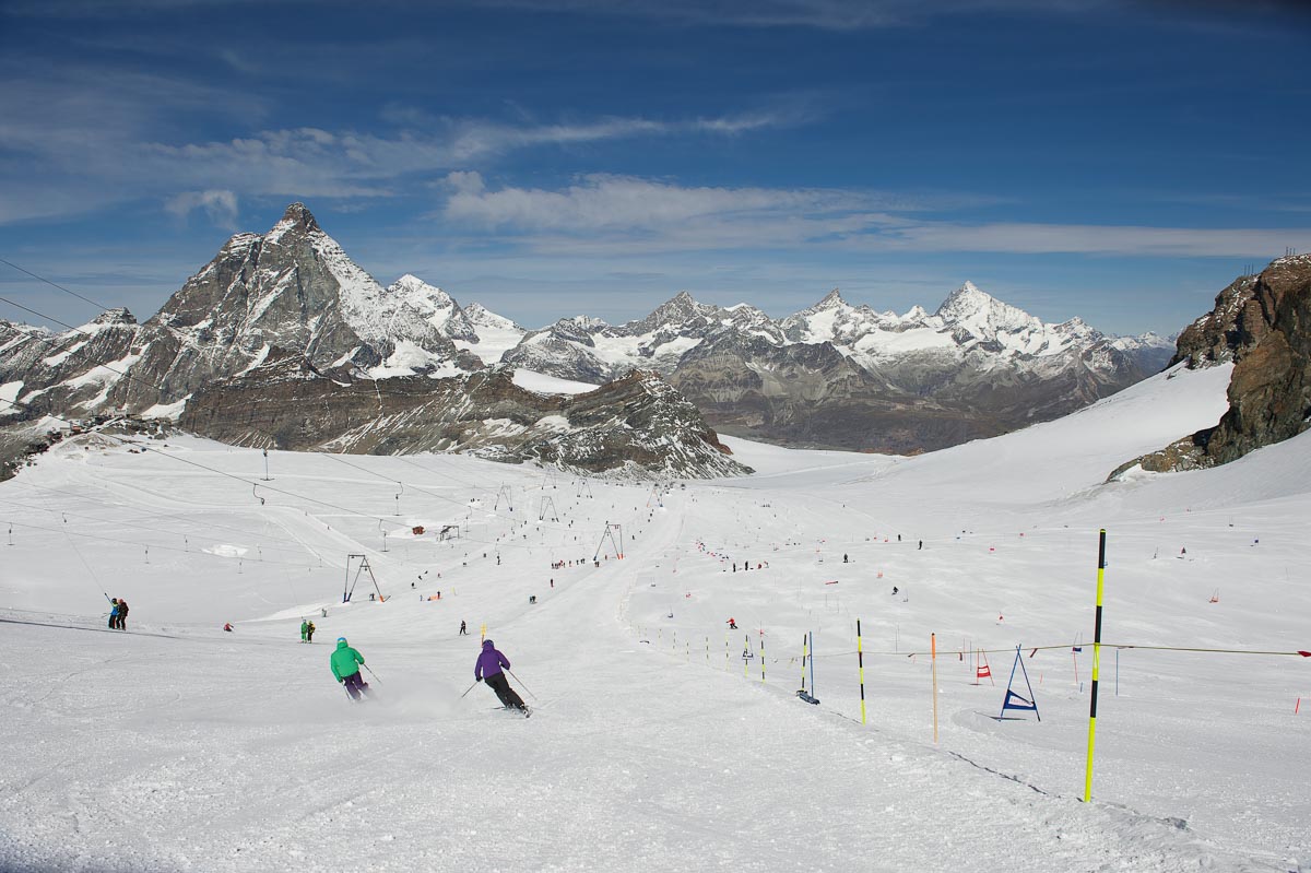 a summer glacier ski area, photographing downhill as skiers ski down the long, gentle slope